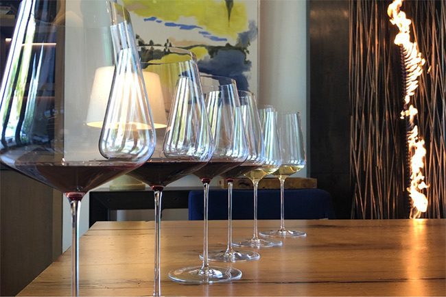 close-up of six wine glasses lined up on a wood table with the same amount of wine.