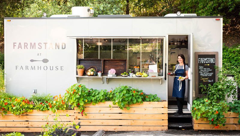 The Farmstand restaurant: small building with Farmstand painted on it and woman standing in doorway holding food.