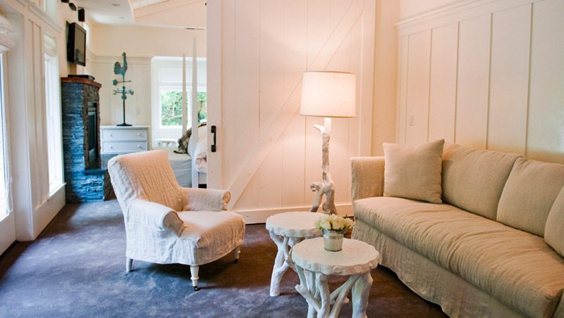 Interior of Barn One Bedroom Suite: White wood partition sliding door in back, white cushioned chair and loveseat with white corner lamp and two small coffee tables.