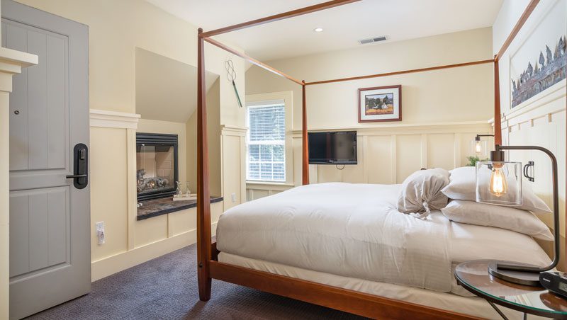 Interior of Farmhouse room: large bed with brown wood bedframe and bed posts, ornate wood moulding on walls and farmed picture on wall.